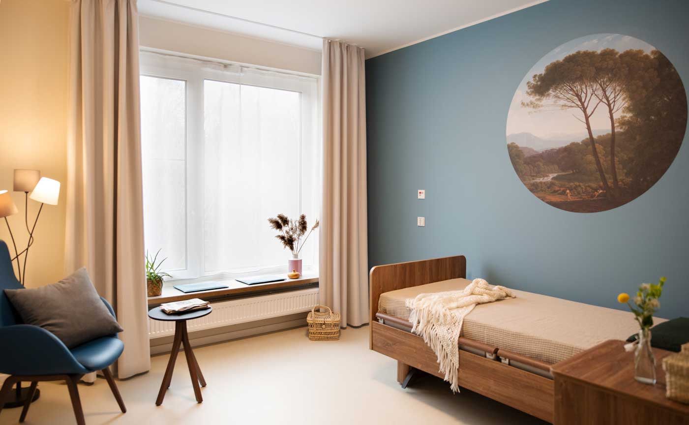 Zimmer Pflegeheim blaue Wand mit runder Tapete über dem Bett gemütliche Leseecke mit Sessel und Stehleuchte