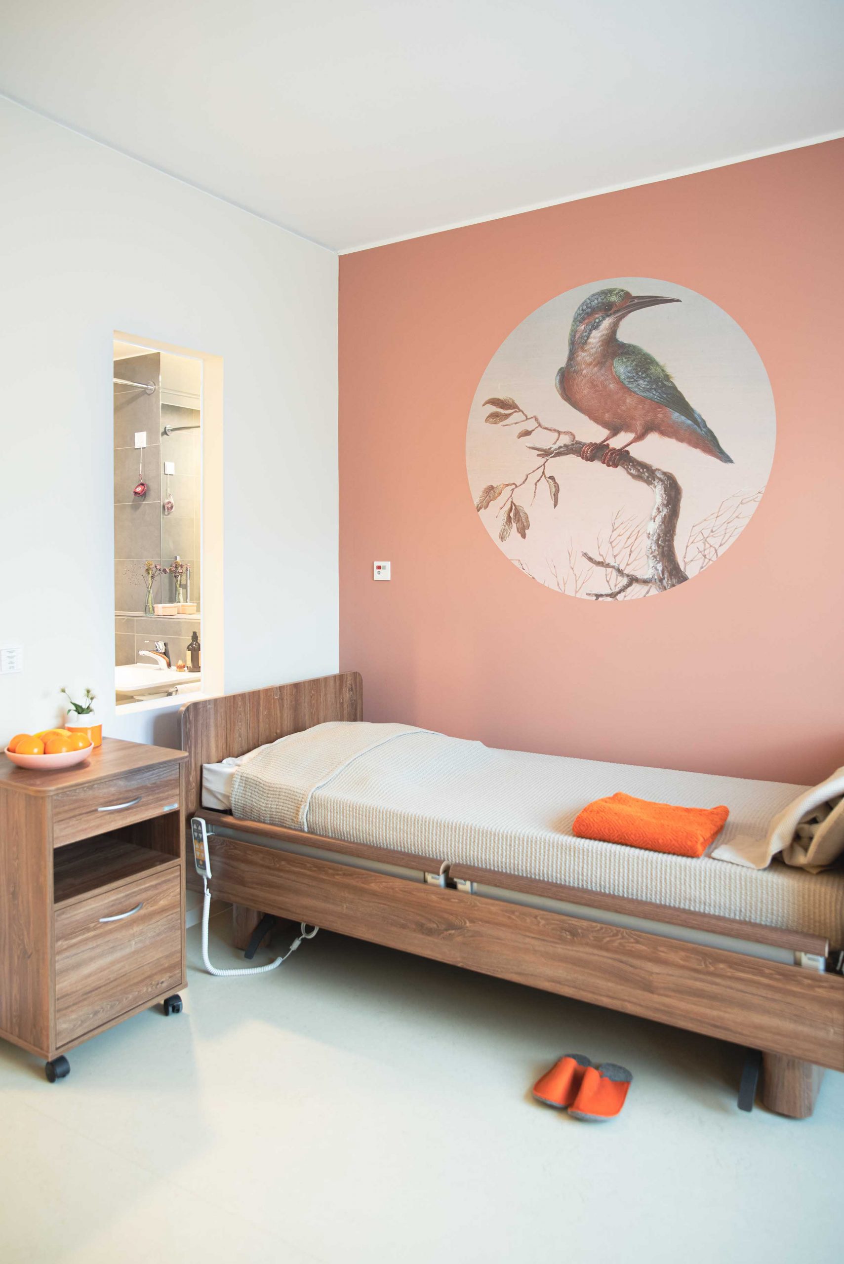 Wilkening_Zimmer_Vogel_BettBad Bewohnerzimmer mit Eisvogel auf runder Tapete Blick ins beleuchtet Badezimmer