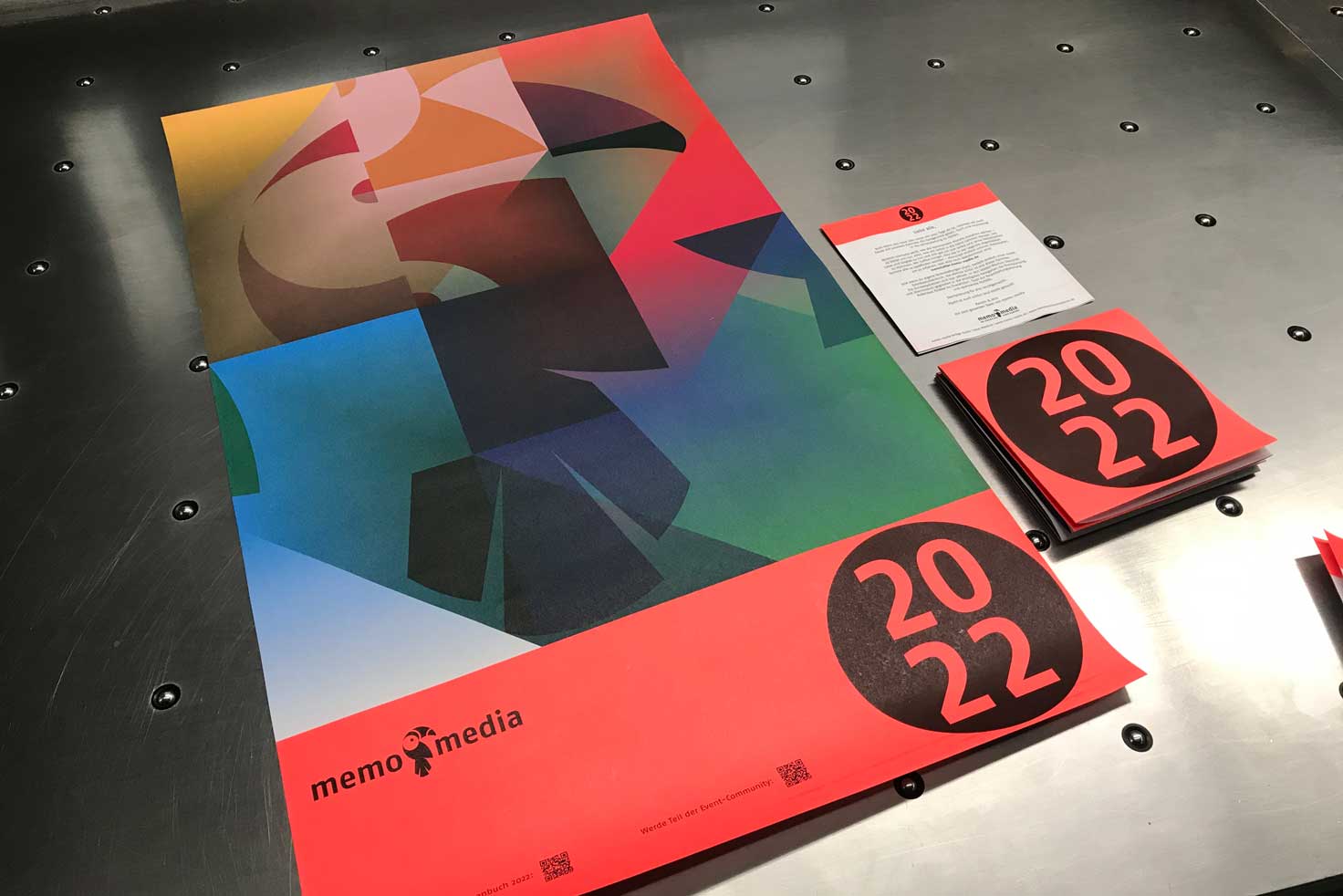 kalender_memo-media-andruck Wandkalender memo-media bunte Vorderseite auf Druckmaschine daneben gefalteter Kalender und Anschreiben